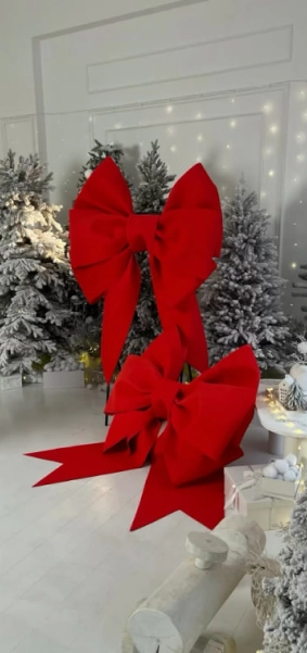 Large decorative red bows made of foamiran displayed in a holiday setting with Christmas trees